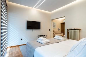 Ein modernes Hotelzimmer mit einem an der Wand befestigten Flachbildfernseher, einem Bett mit ordentlich gefalteten Handtüchern, einem Heizkörper und einem Holzboden.