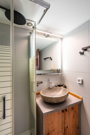 Ein modernes Badezimmer mit Duschkabine aus Glas, einem Holzschrank und einem runden Waschbecken aus Stein.