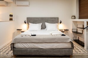 Ein ordentlich bezogenes Bett mit grauem Kopfteil, weißer Bettwäsche und zwei Nachttischlampen.
