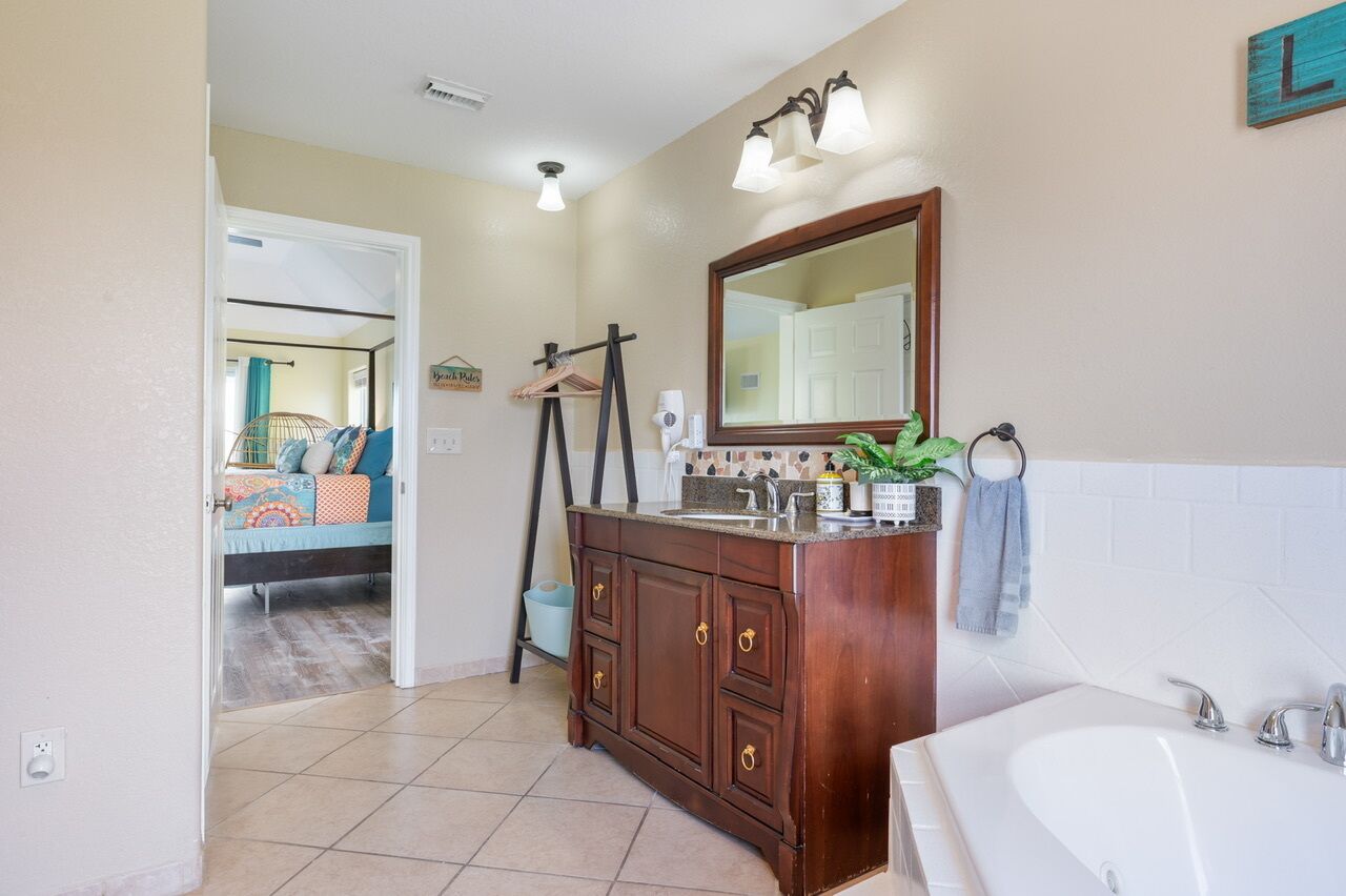 A bathroom with a large mirror, a sink, and a bathtub. There is a towel rack and a towel hanging on it.