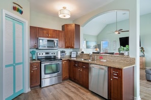 A kitchen with wooden cabinets, stainless steel appliances, a granite countertop, and a ceiling fan. - Sol Searcher - Close to the beach, gulf view, easy beach access! (Crystal Beach)