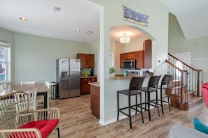 A spacious kitchen with modern appliances, a dining area with wicker chairs, and a staircase leading to an upper level. - Sol Searcher - Close to the beach, gulf view, easy beach access! (Crystal Beach)