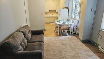 A compact living space with a sofa, a dining table with chairs, and a kitchen area with cabinets and appliances.