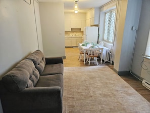 Un espace de vie compact comprenant un canapé, une table à manger avec des chaises et un coin cuisine avec des placards et des appareils électroménagers.