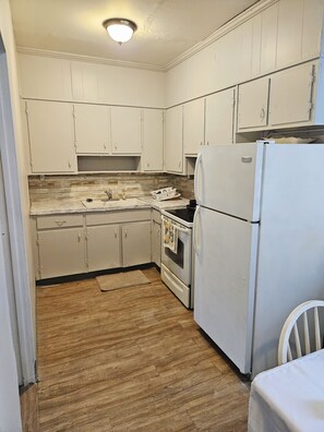 A compact kitchen with white cabinets, a white refrigerator, and a wooden floor.