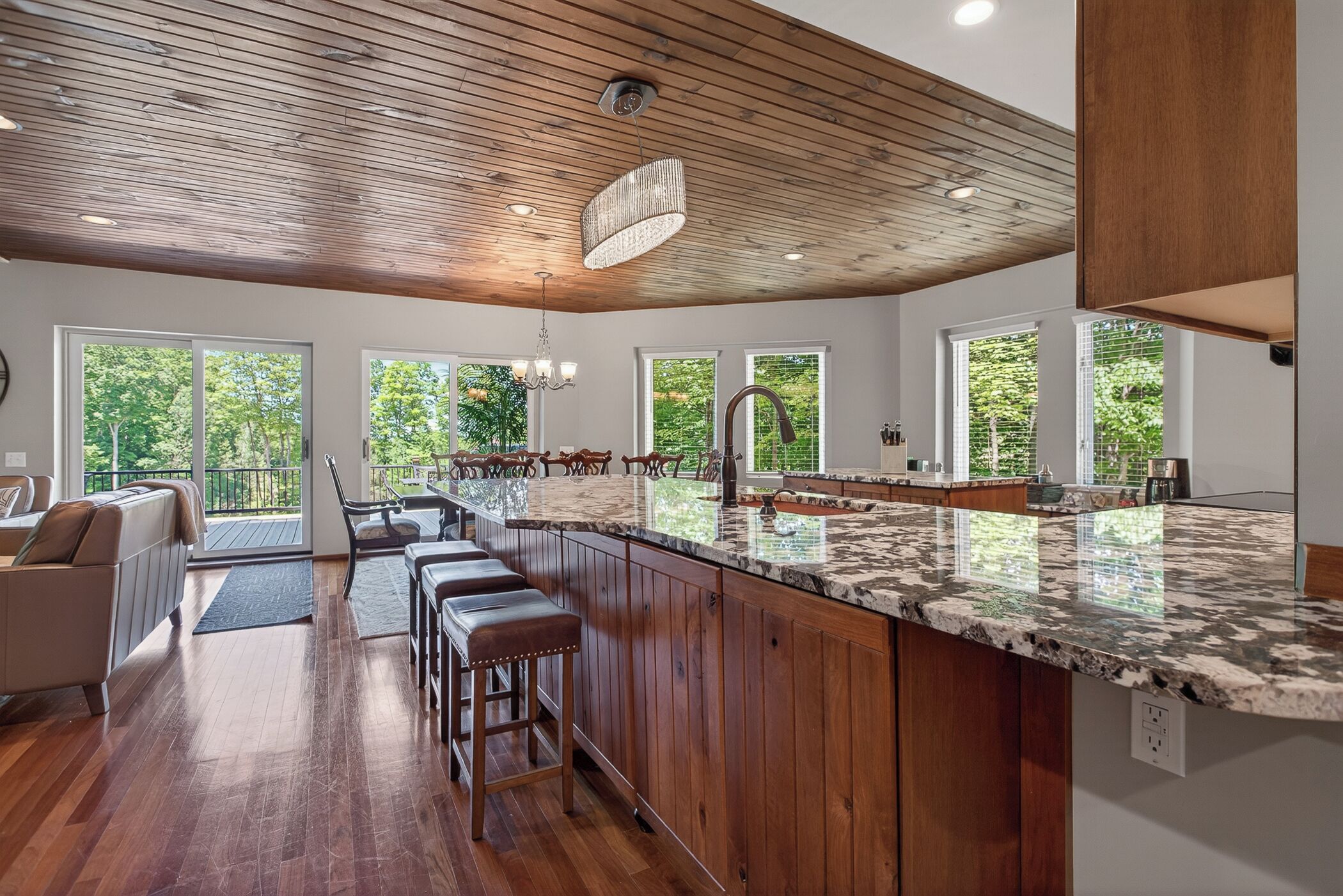 A spacious kitchen with a wooden ceiling, large windows, and a marble countertop.