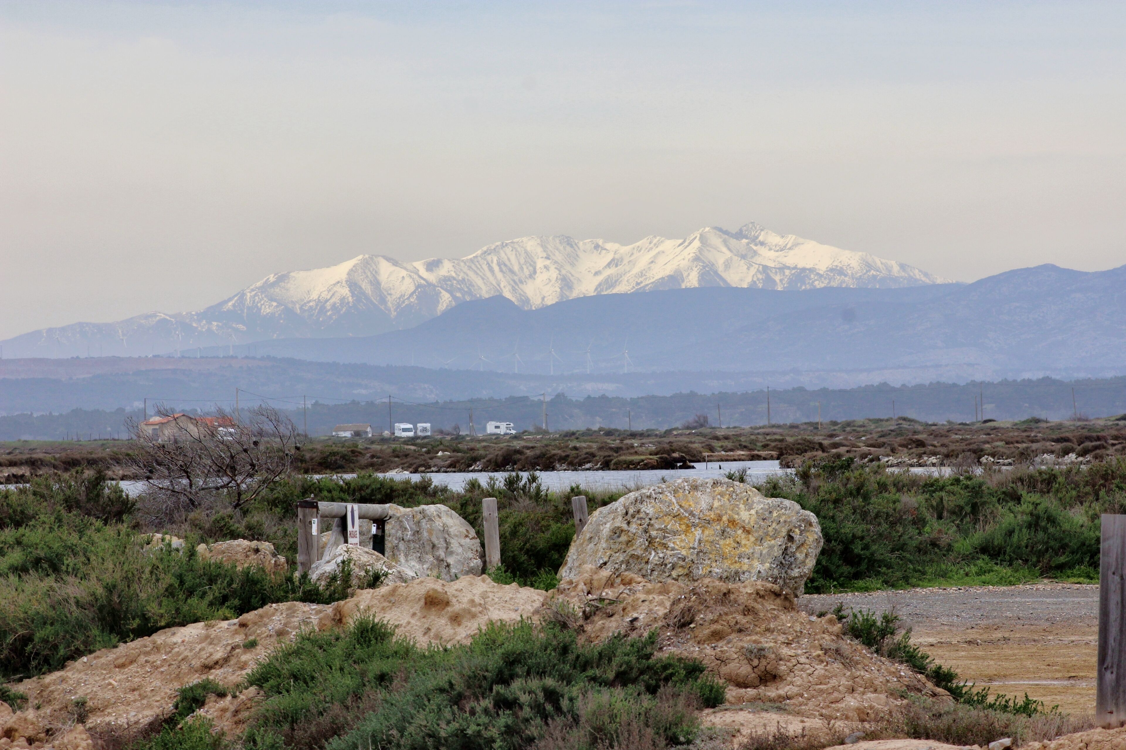Paisaje montañoso con picos nevados, una masa de agua y terreno rocoso.
