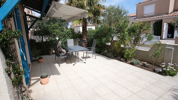 Une terrasse extérieure avec une table et des chaises, entourée de plantes en pot et agrémentée d’une pergola.