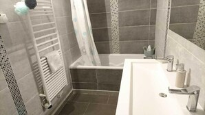A bathroom with a bathtub, a shower curtain, a towel rack, and a sink with a mirror. - Spacious apartment near downtown (Avignon)