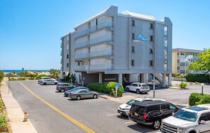 Ein mehrstöckiges Hotel mit Parkplatz, blauem Himmel und Blick auf den Strand.