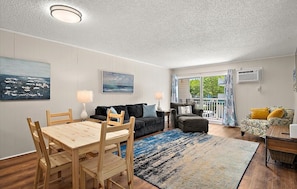 Ein gemütliches Wohnzimmer mit Esstisch, Sofas und einem großen Fenster mit Vorhängen.