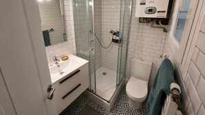Ein Badezimmer mit Duschkabine, Waschbecken mit Spiegel, Toilette und Handtuchhalter.