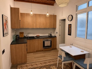 Una cocina compacta con armarios de madera, una encimera negra, un lavamanos, un tostador y un reloj en la pared.