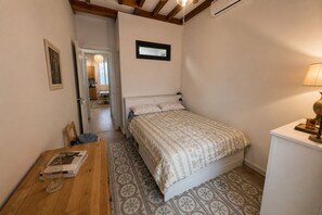 Un dormitorio con cama, escritorio, silla, lámpara y puerta que da a otra habitación.