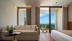 Habitación de hotel moderna con sofá, cama, una mesita con un libro y vistas al exterior.