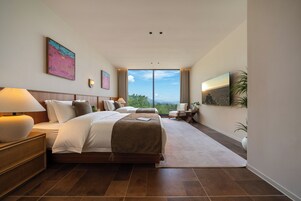 Quarto de hotel moderno com uma cama grande, uma mesa, uma cadeira e vista para o exterior.