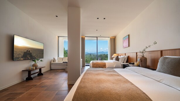 Una habitación de hotel moderna con una cama grande, un televisor de pantalla plana, un ventanal con vistas a la ciudad y un cabecero de madera.