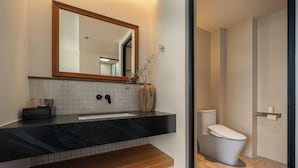Un baño moderno con encimera de mármol negro, tocador de madera, inodoro blanco y espejo sobre el lavabo.