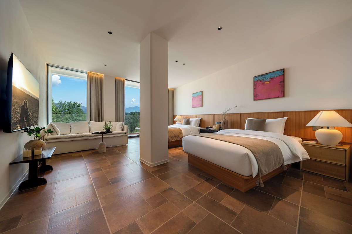 A modern hotel room with a large bed, a sofa, a TV, and a window with curtains.