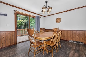 A dining room with a wooden table and chairs, a chandelier, a clock on the wall, and a view of the outdoors. - Balsam Lodge, our newly renovated addition to Hillcrest Cottages. (St.Germain)