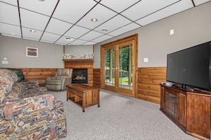 A log cabin interior with a sofa, fireplace, television, and a large window. - Balsam Lodge, our newly renovated addition to Hillcrest Cottages. (St.Germain)