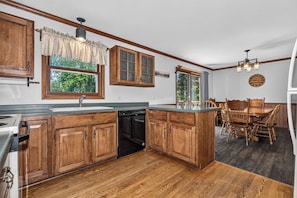 A kitchen with wooden cabinets, a dishwasher, a dining table with chairs, and a window with a view of trees. - Balsam Lodge, our newly renovated addition to Hillcrest Cottages. (St.Germain)