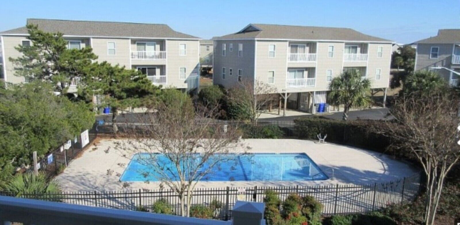 A residential building with a swimming pool, surrounded by trees and a fence.