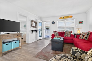 A living room with a TV, red sofa, patterned ottoman, and a starfish rug. - Salt & Sound -  Top Floor Water Views - Walk to Beach - 3 Bedroom 2 Bathroom (Ocean Isle Beach)