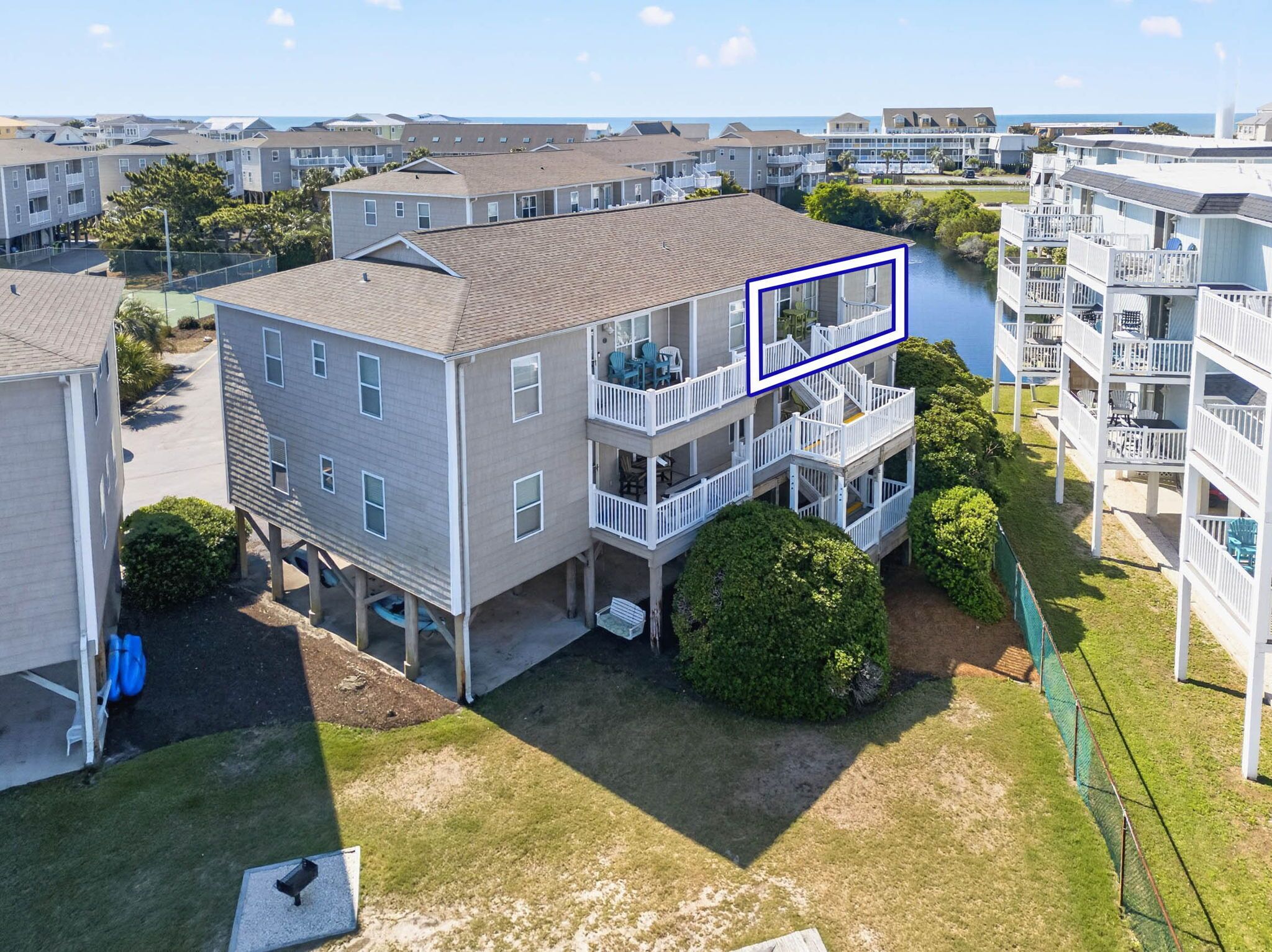 A multi-story residential building with balconies, a lawn, and a body of water in the background.
