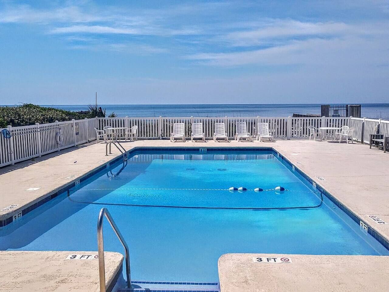 Una piscina rettangolare con ringhiera metallica, indicatore di profondità di 3 piedi e sedie a sdraio lungo il bordo vasca.