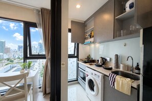 A modern kitchen with a washing machine, a dining area with a view, and a cityscape visible through the window. - 5 min to BTS Fully Equipped Kitchen with City View (Khet Khlong Toei)