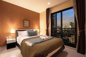 A hotel room with a large bed, a city view, and a nightstand with a lamp. - 5 min to BTS Fully Equipped Kitchen with City View (Khet Khlong Toei)
