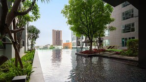 Ein modernes Gebäude mit einem spiegelnden Pool, umgeben von Grünflächen und einem hohen Wolkenkratzer im Hintergrund.