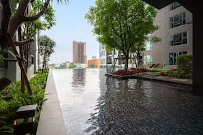 Ein modernes Gebäude mit einem spiegelnden Pool, umgeben von Grünflächen und einem hohen Wolkenkratzer im Hintergrund.