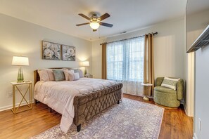 A bedroom with a bed, two bedside tables, a floor lamp, a ceiling fan, a window with curtains, and a green armchair. - Great for Families! Raleigh Townhome 5 Mi to Dtwn (Raleigh)