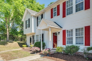 A two-story house with a front porch, a red door, and a small front yard with plants. - Great for Families! Raleigh Townhome 5 Mi to Dtwn (Raleigh)
