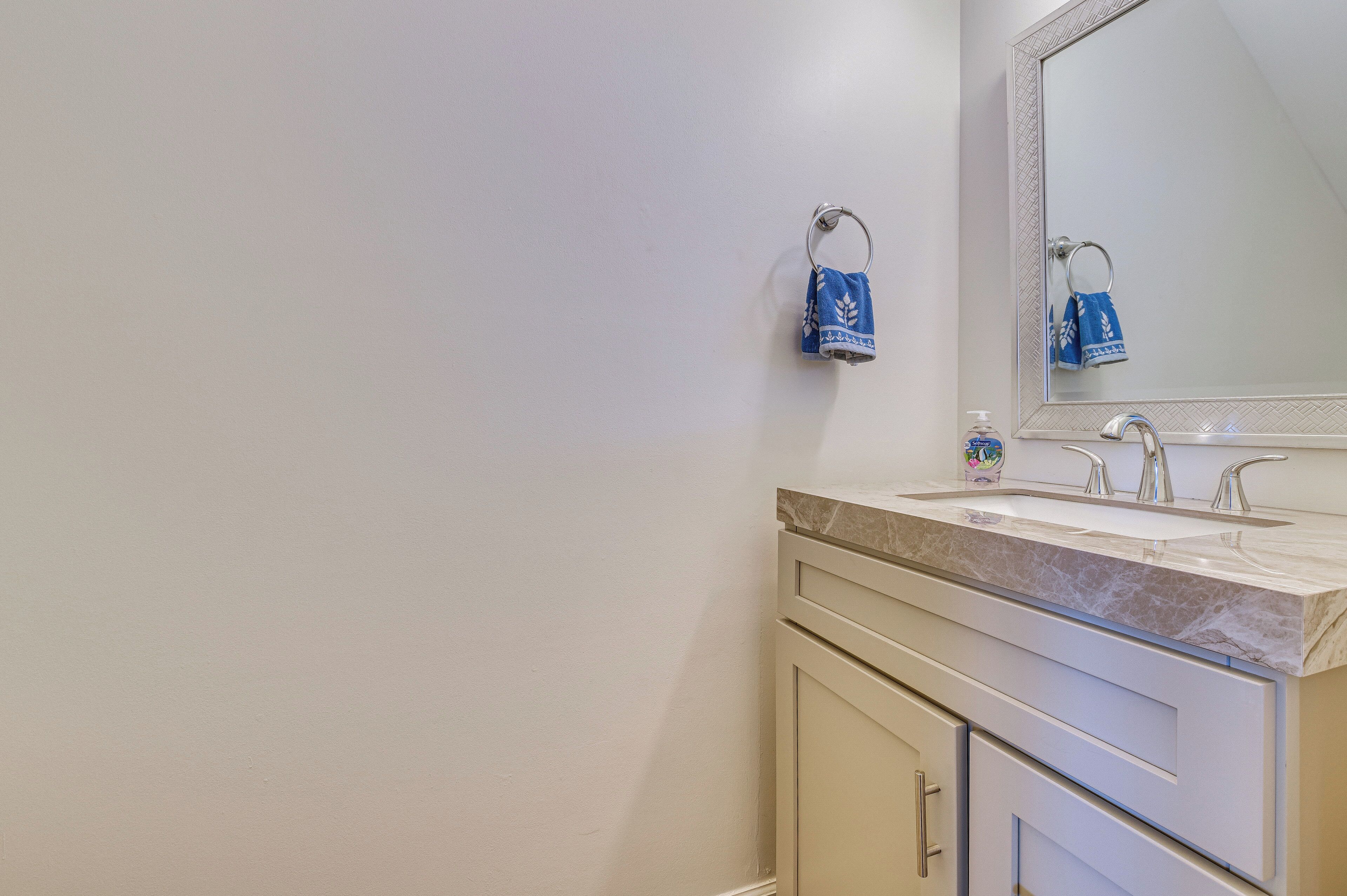 A bathroom with a marble countertop, a sink, a mirror, and a towel rack with a blue towel.
