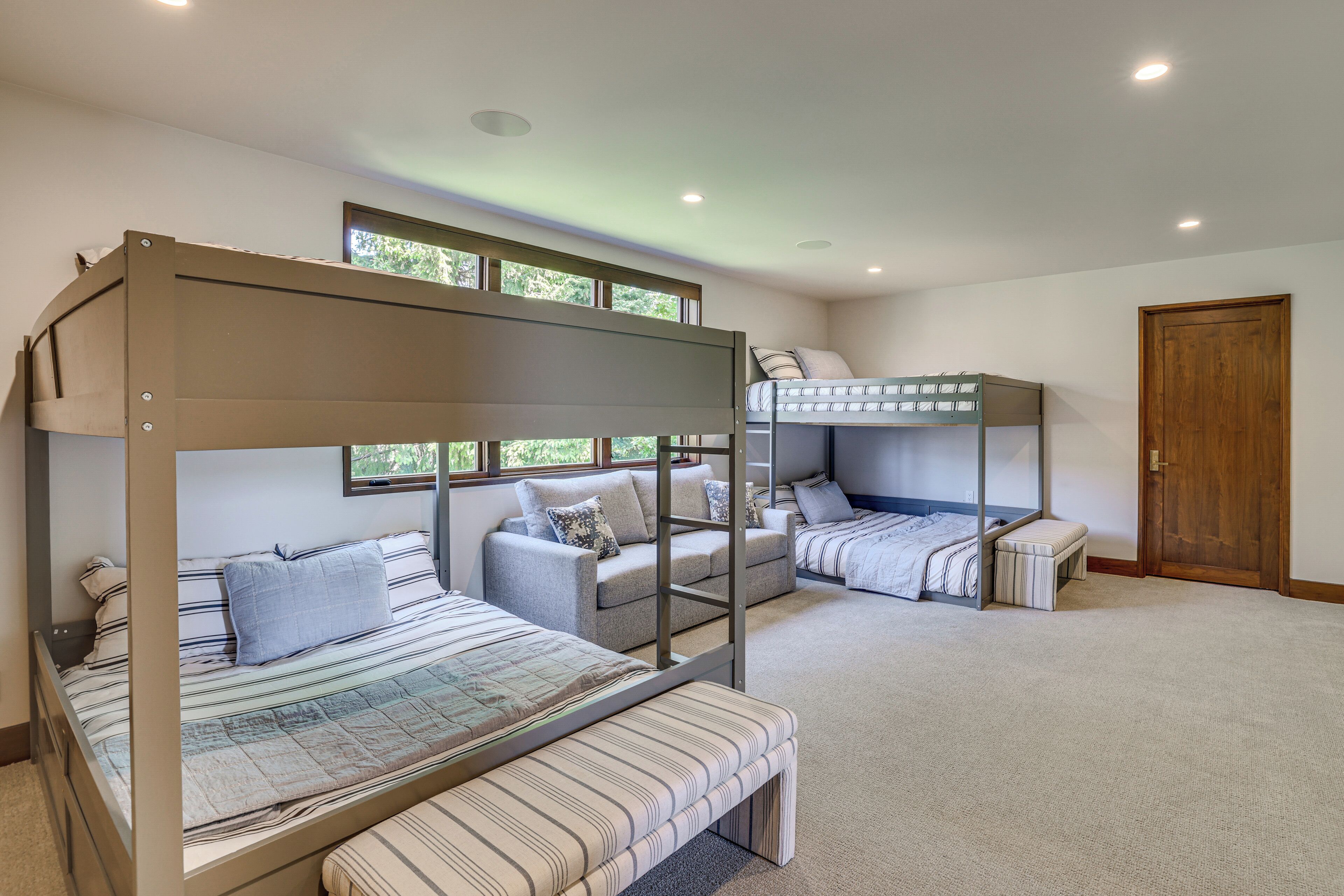 A bunk bed room with a sofa and a bench, a wooden door, and a window.