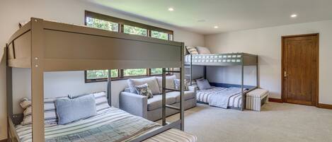 A bunk bed room with a sofa and a bench, a wooden door, and a window.