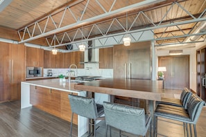 A modern kitchen with wooden cabinets, a central island with bar stools, and pendant lighting. - Grand Haven Condo w/ Channel View & Dtwn Location (Grand Haven)