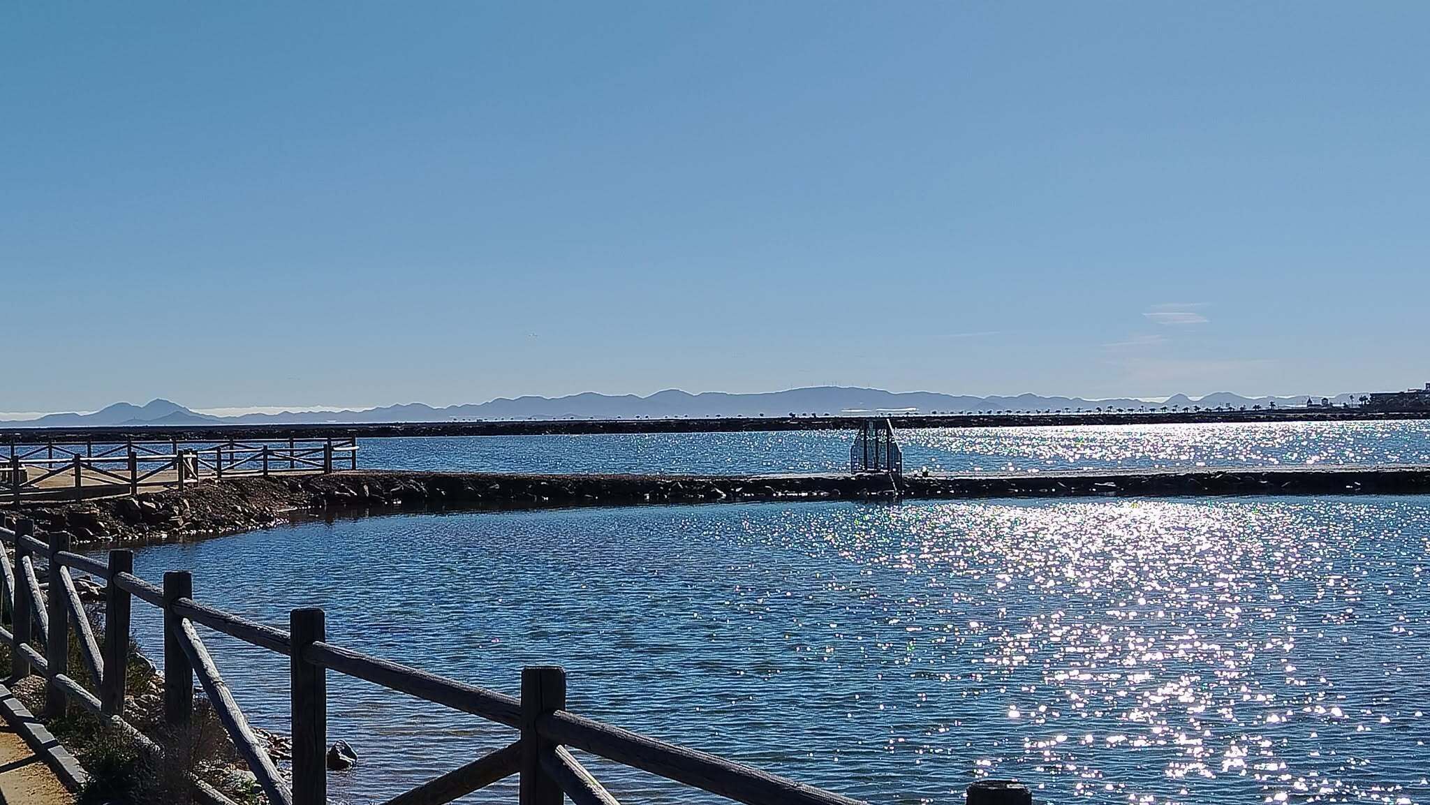 A coastal view with a wooden pier, calm water, and distant mountains.