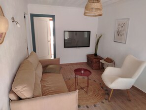 A living room with a sofa, a white armchair, a TV, a small table, and a wicker basket. - Maison typique de San Pedro del Pinatar : Plages et toutes commodités à pied ! (San Pedro del Pinatar)