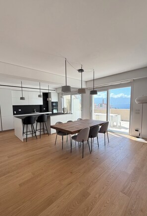 Eine moderne Küche mit einer zentralen Kochinsel, einem Essbereich mit Holztisch und -stühlen sowie Meerblick durch große Fenster.