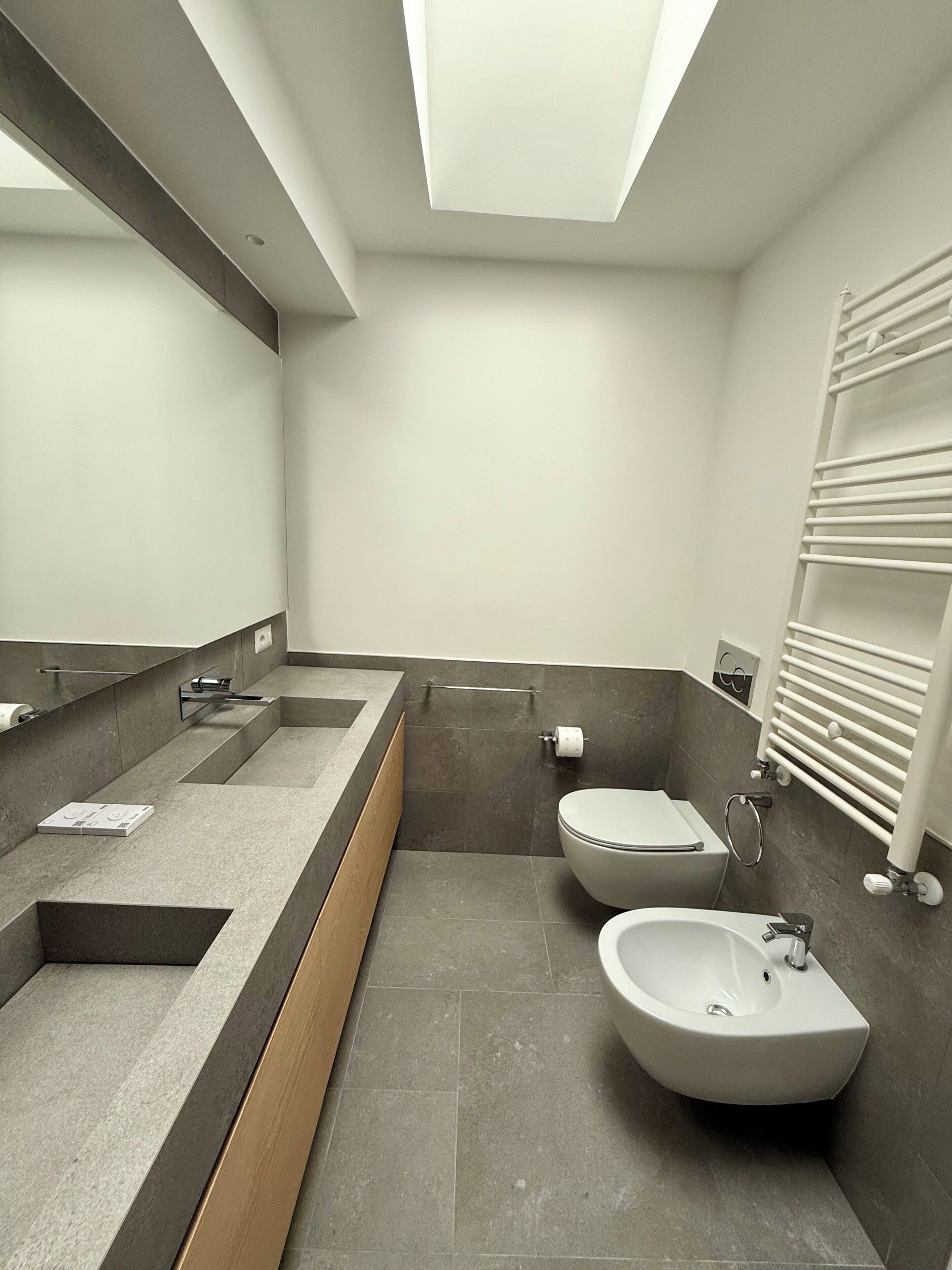 A modern bathroom with a large mirror, a bidet, a toilet, and a towel rack.