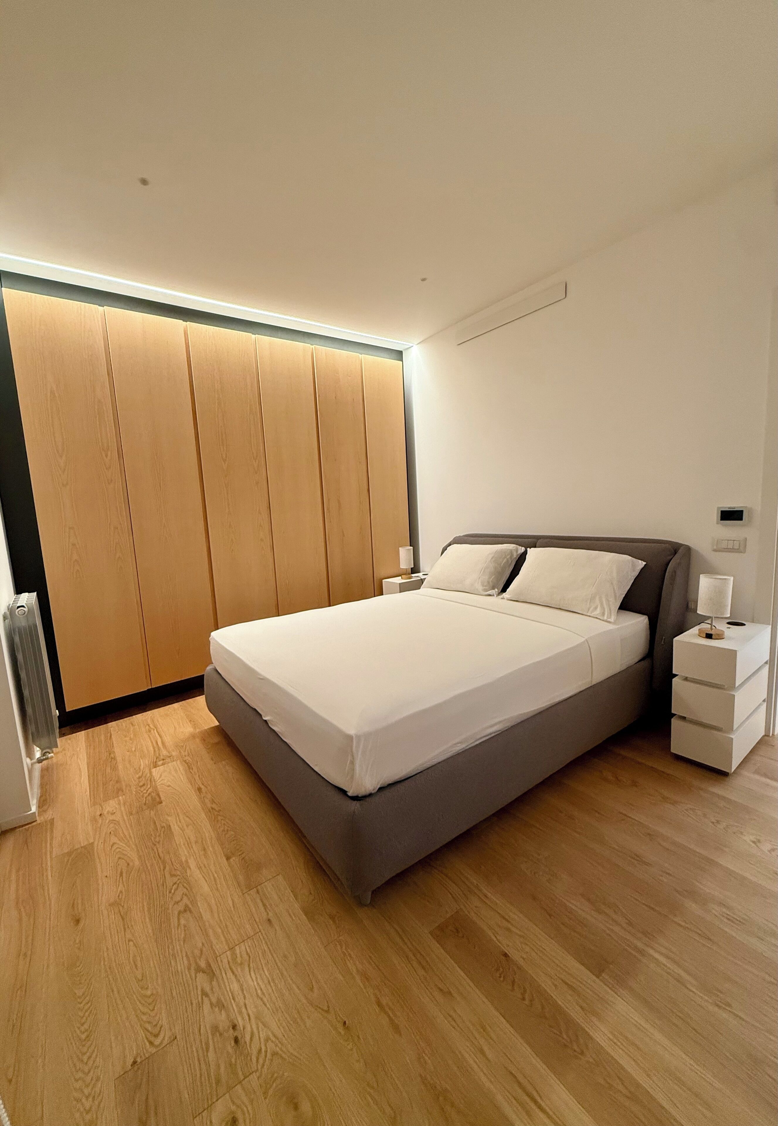 A modern bedroom with a large bed, wooden wardrobe, and bedside tables.