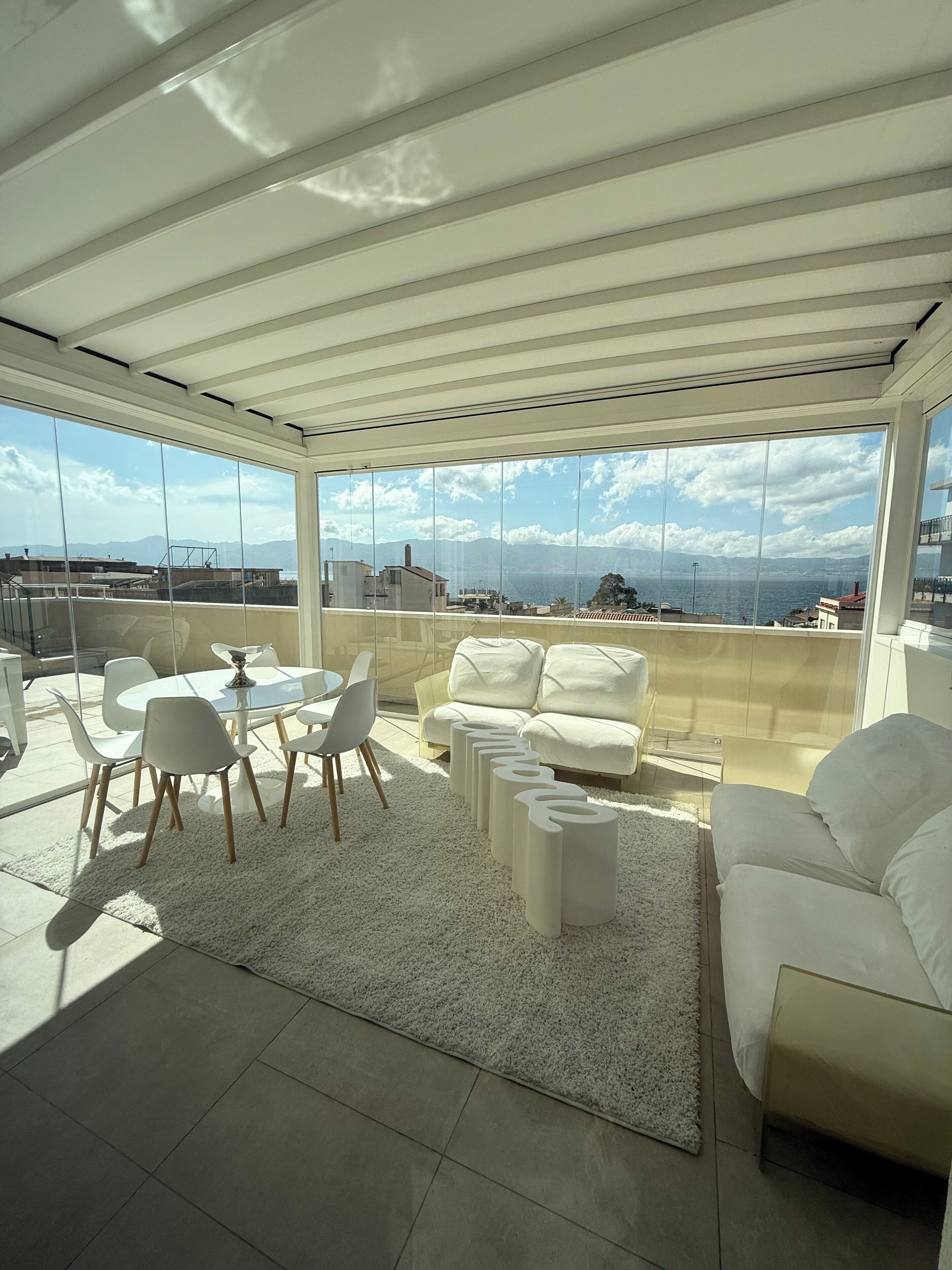 Un balcon spacieux avec un plafond blanc, une table ronde entourée de chaises, un canapé et un tapis.