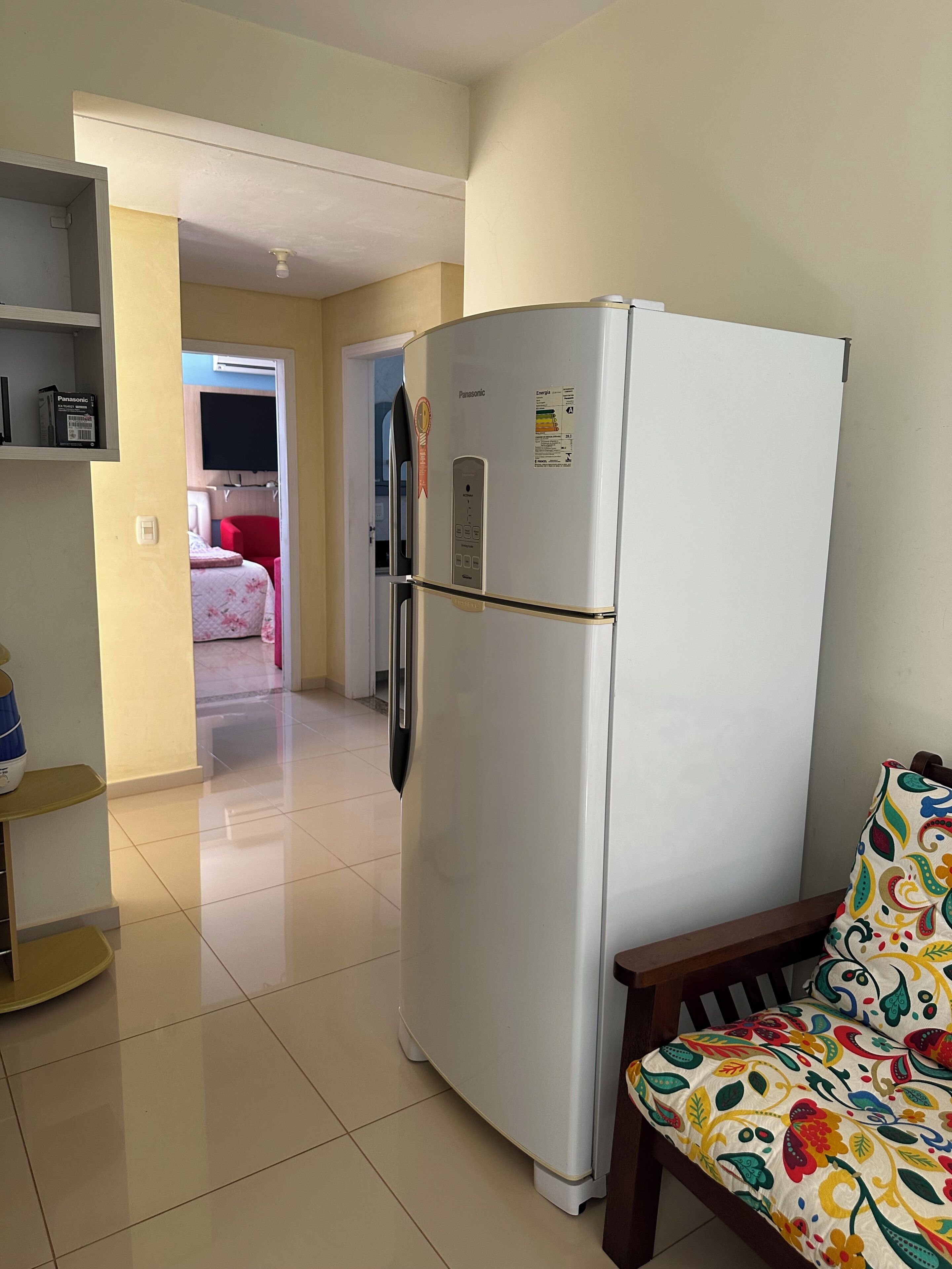 A white refrigerator with a control panel, a wooden bench with a colorful cushion, and a tiled floor.