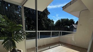 Un balcón con una maceta, un tapete tejido y vistas a árboles y edificios.