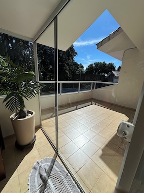 A balcony with a potted plant, a woven mat, and a view of trees and buildings. - Recanto Luna foz (Foz do Iguaçu)
