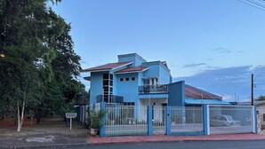 Una casa de dos pisos con techo de tejas rojas, cerca blanca y camino de entrada pavimentado.